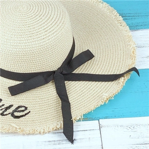 Detail of summer straw hat featuring black ribbon bow and embroidered brim lettering