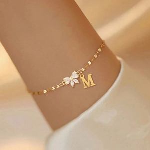 Close-up of elegant gold letter M bracelet with zircon flower charm on woman's wrist