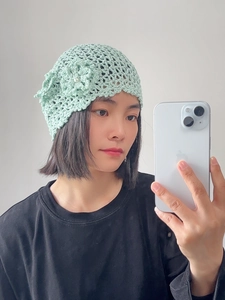 Close-up of mint green hand-crocheted hat featuring a 3D floral accent and pearl bead