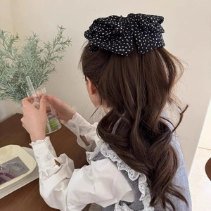 Gros plan d'une pince à cheveux vintage à pois noirs sur des cheveux bruns ondulés