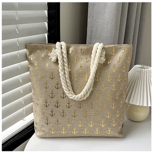 Detail of beige linen tote bag featuring golden anchor prints and rustic rope handles