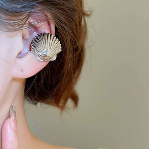Macro detail of gold shell ear cuff with fine radiant texture worn on female model's ear