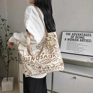 Detail of canvas tote bag featuring brown cartoon dinosaur print and fabric shoulder strap