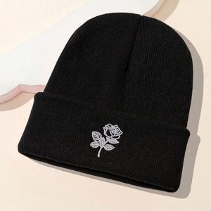 Close-up of fine black knit beanie featuring a white rose embroidery on the folded brim