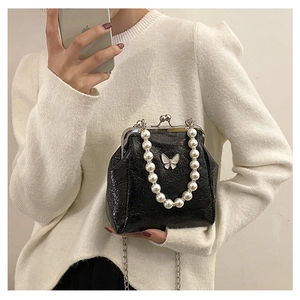Detail of black pleated glossy leather bag with pearl handle and silver butterfly charm