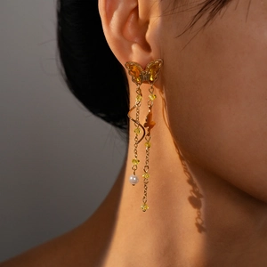 Detail of gold butterfly tassel earrings with yellow crystals and elegant pearl drop