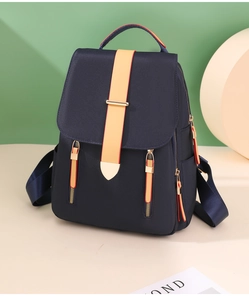 Detail of dark blue nylon backpack with orange contrast straps and metal snap button closures