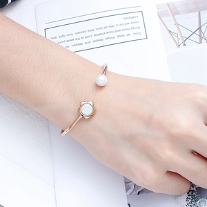 Detail of rose gold C-shaped cuff bracelet with white flower and pearl on a model wrist