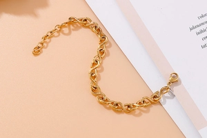 Polished gold infinity chain bracelet with lobster clasp on a minimalist beige backdrop