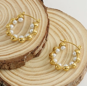 Detailed view of 18k gold plated hoop earrings with white pearls on rustic wood slices