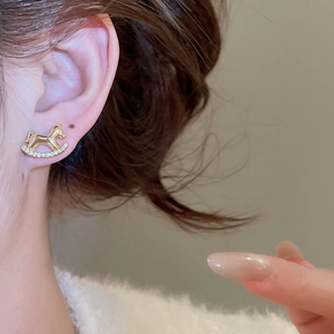 Détail d'une boucle d'oreille cheval à bascule dorée avec zircons sur le mannequin
