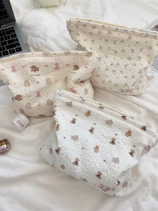 Three quilted makeup bags with floral and bear patterns on a bed with a laptop