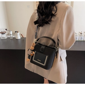 Detail of black bucket bag with wide ethnic strap and bunny charm accessory
