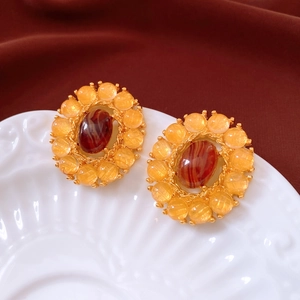 Macro shot of vintage gold earrings with oval red agate and amber beads on a porcelain tray