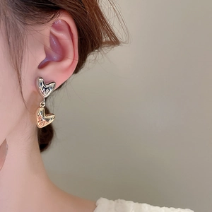 Close-up of elegant double heart metallic earrings worn on ear with silver finish