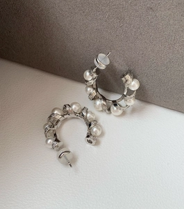 Macro shot of silver C-shape earrings with pearls and zircon crystals on velvet surface