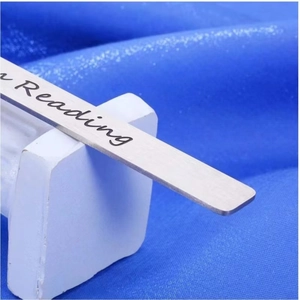 Macro shot of stainless steel bookmark with engraved reading script on blue fabric