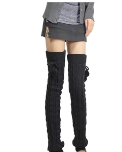 Detail of black cable knit over-knee leg warmers with fuzzy pom-poms on long socks
