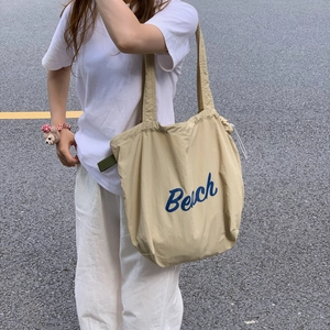 Close-up of beige canvas tote bag featuring blue Beach lettering print on white t-shirt