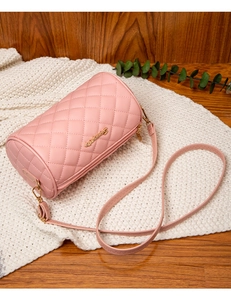 Detail of pink quilted cylinder crossbody bag with gold hardware on white knit texture