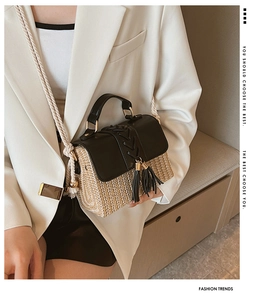 Detail of hand-woven straw handbag featuring black leather trim and decorative fringe tassels