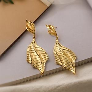 Detail shot of golden maple leaf earrings with textured metallic surface on books