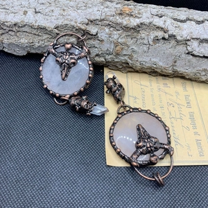 Macro detail of retro bronze earrings featuring bull skull, rose quartz, and crystal points