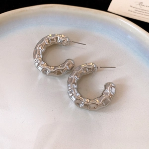 Macro shot of silver C-shaped hoop earrings with irregular hammered metal texture on ceramic