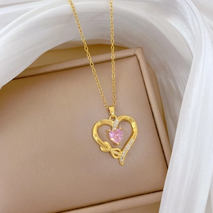 Close-up of golden heart necklace with pink gemstone and zircon on silk fabric