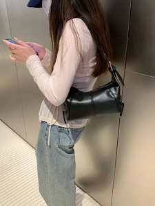 Chic black leather cylinder underarm bag with silver hardware on a female model