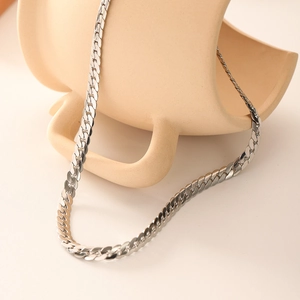 Polished silver stainless steel flat snake chain necklace draped on ceramic decor