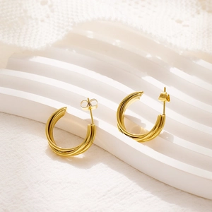 Detail view of triple-layered golden C-shaped hoop earrings on a marble display