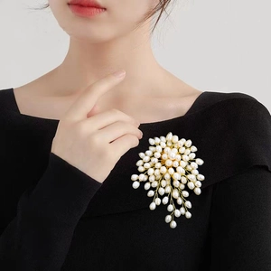 Elegant floral cluster brooch featuring white pearls and gold wire on a black garment