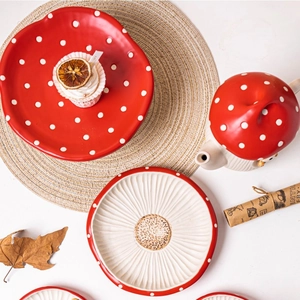 Flat lay of red mushroom ceramic plates and teapot with autumn leaves and woven placemats