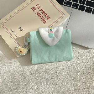 Close-up of mint green fabric card holder with white plush flap and yellow bear charm