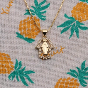 Golden Hamsa Hand necklace with Virgin Mary medal and zircon border on patterned fabric