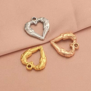Macro detail of heart-shaped wing pendants in gold, silver, and rose gold on pink fabric