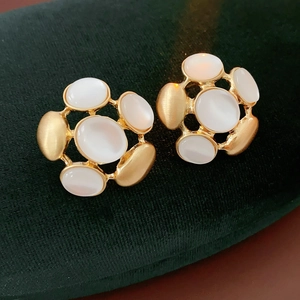 Macro shot of vintage gold flower earrings with white oval stones on green velvet background