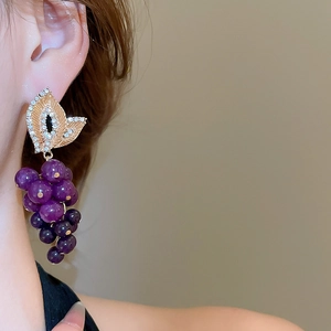 Gros plan de boucles d'oreilles raisin violettes avec détails en cristal doré sur l'oreille