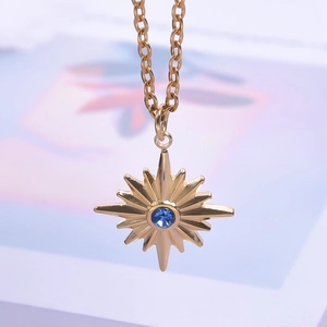Macro detail of a golden starburst pendant necklace with a blue center rhinestone