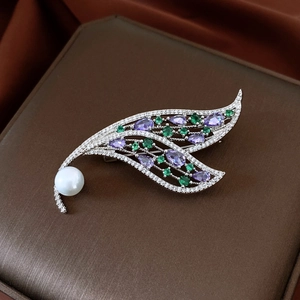 Macro detail of leaf-shaped brooch with inlaid purple gems, emeralds, and a large white pearl