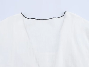 Détail de l'encolure blanche avec passepoil noir et coutures de précision soignées
