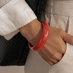Close-up of wide polished red resin bangle worn by a model with a minimalist outfit