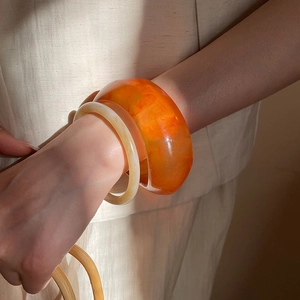 Iridescent orange resin bangle and cream jade-style slim bracelet worn on wrist