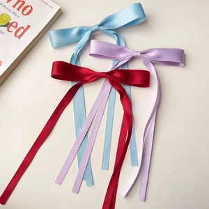 Close-up of red, light blue, and light purple satin ribbon bow hair clips on plain background