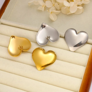 Macro shot of gold and silver heart-shaped stud earrings in a beige velvet jewelry box