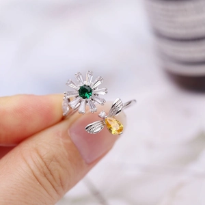 Detail of adjustable open ring featuring rotating bee and daisy with colored gemstones