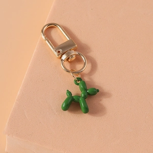 Detail of a shiny green balloon dog keychain with golden metal clasp on a textured surface
