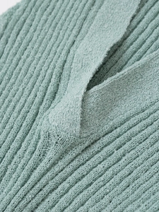 Detailaufnahme von hellgrünem Strickstoff mit Bouclé-Struktur und weichem Kragendetail