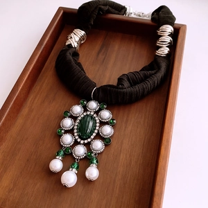 Detailed close-up of oval green gemstone pendant with pearls and black fabric neck strap